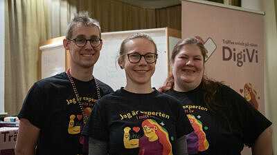 En man och två kvinnor står bredvid varandra och tittar på kameran. De alla har på sig samma t-shirt som visar illustration på en person med håret regnbågsfärgat. Ovanför illustrationen står texten: "jag är experten i mitt liv".