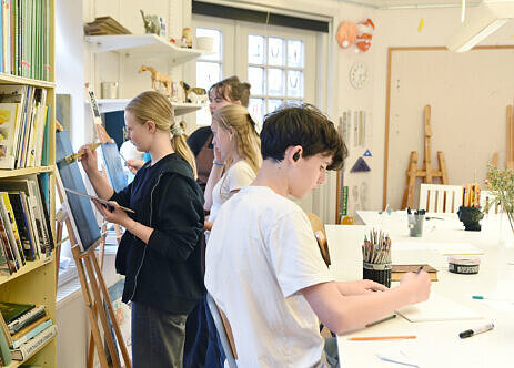 Pojke och flickor som målar och ritar i ateljé