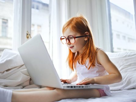 Bild på ett barn med glasögon som sitter med en laptop i knät.