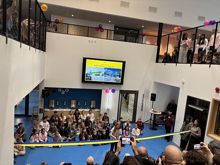 Inomhus miljö salleruppskolan, barn klipper av invigningsband. elever och lärare samlade runt