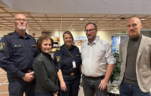 Fem personer, två kvinnor och tre män, står i ett reception och tittar in i kameran. Två av dem bär polisuniform.
