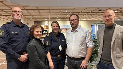 Fem personer, två kvinnor och tre män, står i ett reception och tittar in i kameran. Två av dem bär polisuniform.