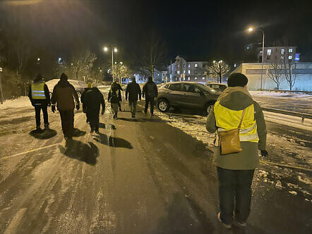 Flera personer i gula västar går i mörker på en gata med ryggen mot kameran